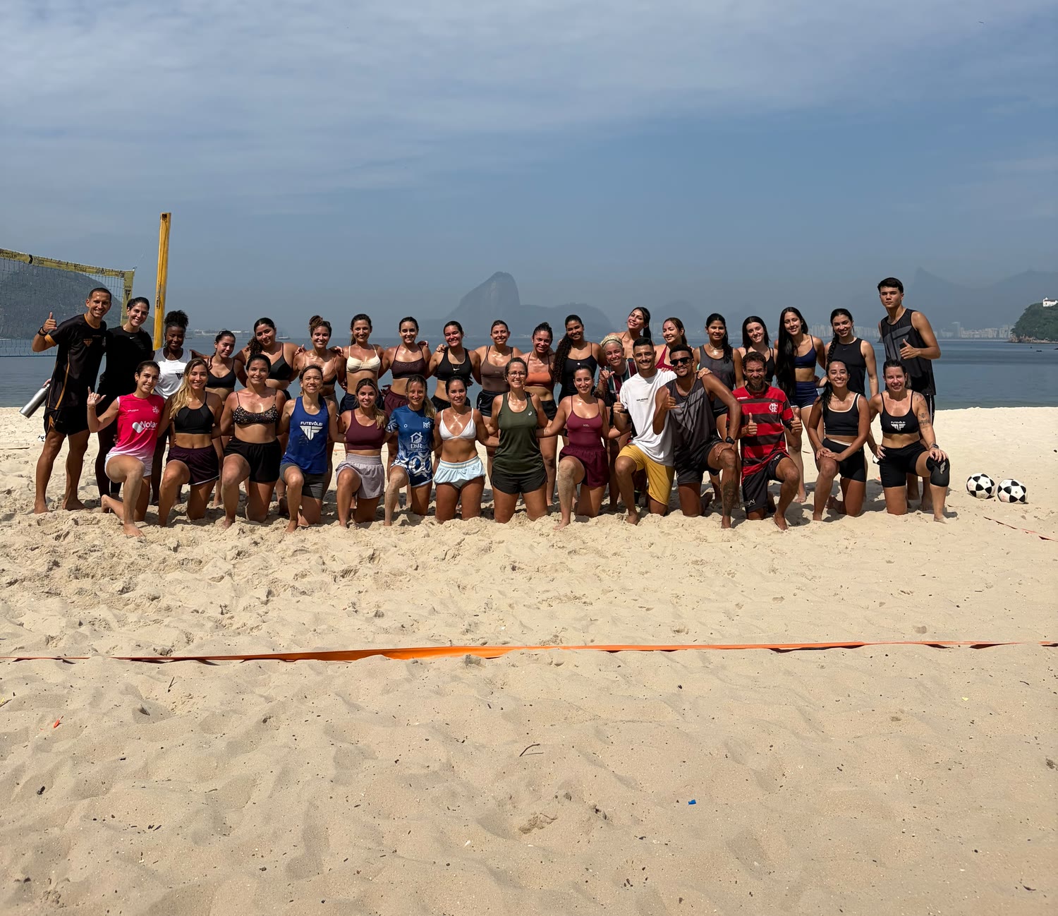 Turma numerosa da MF Futevôlei reunida na areia de Icaraí, com o Pão de Açúcar ao fundo