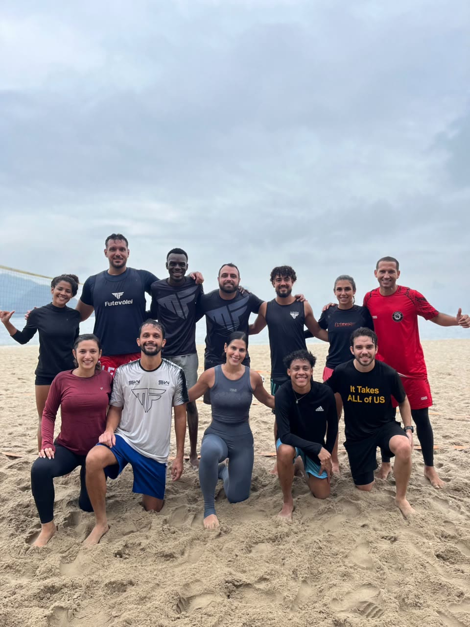 Turma da MF Futevôlei posando de joelhos e em pé na areia em dia nublado